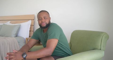 African man sitting relaxed on green armchair in minimalist bedroom interior
