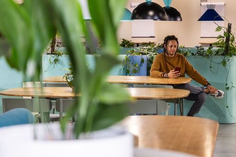 African american man relaxing on planter bench using smartphone in modern coworking lounge