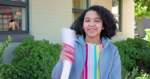 African american teen smiling holding rolled certificate outdoors on school campus