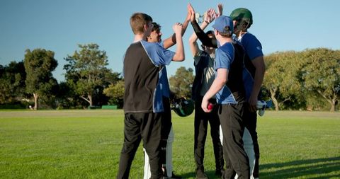 Cricket team high-fiving in huddle celebrating wicket on sunny community sports field