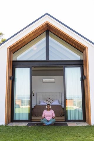 African american woman meditating at modern coastal retreat threshold with sliding doors