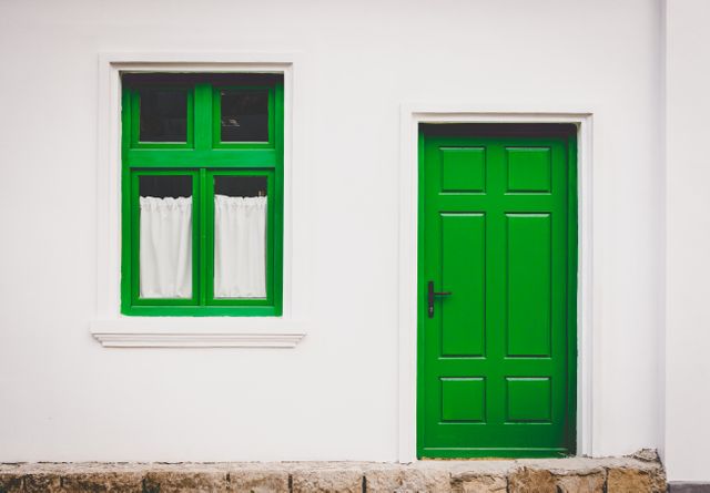 Bright green door and window on a minimalist white wall showcase simple yet striking home exterior design. Ideal for themes on architecture, home and garden, exterior design, traditional housing, and vibrant color usage.