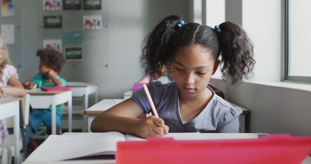 Image of focused biracial girl sitting at desk in classsroom. primary school education and learning concept.