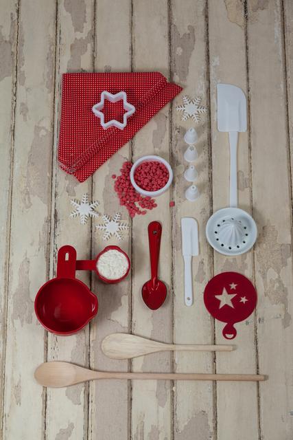 This image showcases a variety of baking tools and ingredients neatly arranged on a rustic wooden surface. The items include wooden spoons, spatulas, a cookie cutter, measuring cups, and dessert toppings. The red and white color scheme adds a festive touch, making it ideal for holiday baking themes. This image can be used for cooking blogs, recipe websites, kitchenware advertisements, or holiday baking promotions.