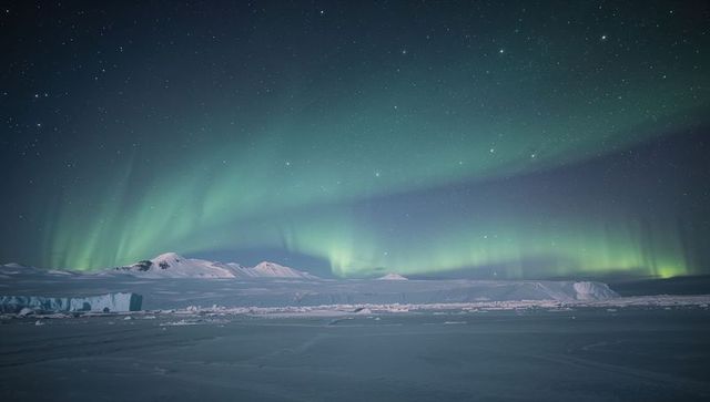 Aurora borealis dancing above arctic icefield and mountains under starry polar night sky