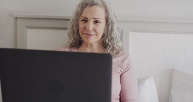 Senior woman with laptop in bed smiling confidently - Download Free Stock Images Pikwizard.com