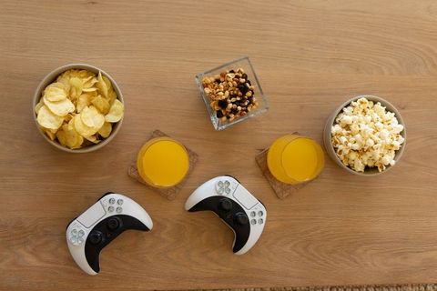 Couple playing console games with controllers, snacks and orange juice on wooden table