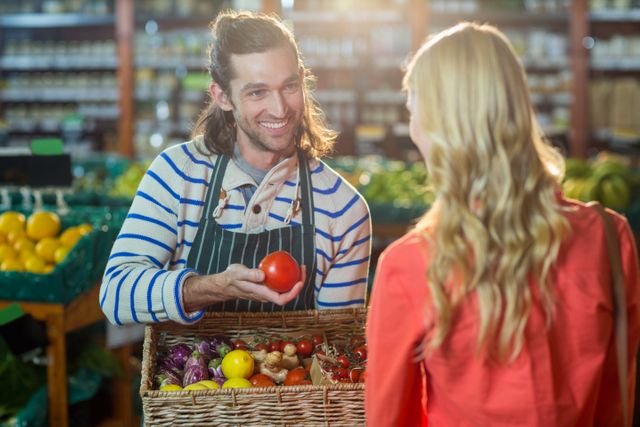 Male staff assisting woman in selecting fresh vegetables in supermarket
