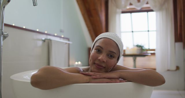 Woman enjoying a relaxing bath in a serene bathroom. The scene conveys comfort, tranquility, and luxury, making it useful for promotions related to wellness, self-care, skincare products, home spa experiences, and lifestyle blogs discussing mindfulness and relaxation techniques.