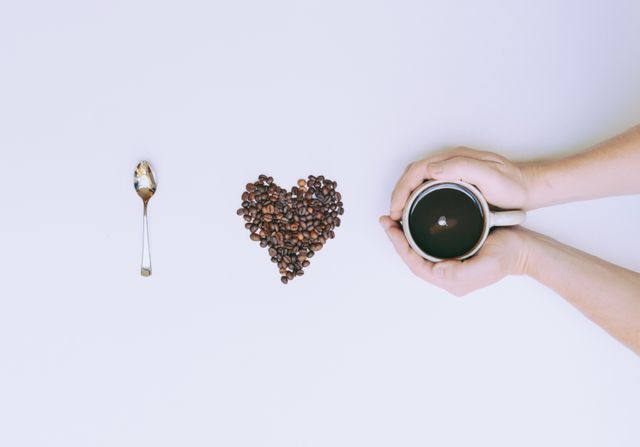 Hands Holding Coffee Cup Beside Spoon and Coffee Beans Heart - Download Free Stock Photos Pikwizard.com