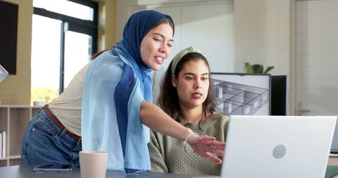 Diverse female colleagues collaborating over laptop with architectural floorplan on monitor