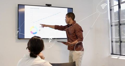 Presenter pointing at growth chart on screen with tablet in modern business meeting room