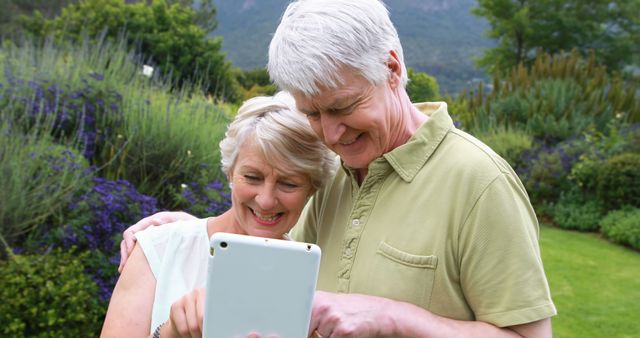 Happy senior couple smiling while using tablet in garden. Ideal for promoting technology use among the elderly, leisure activities for seniors, digital inclusivity, and outdoor living.