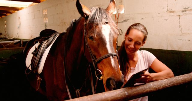 Woman is grooming her horse in a stable, highlighting their bond and mutual affection. Suitable image for articles and advertisements related to animal care, horse riding, equestrian activities, and veterinary services.
