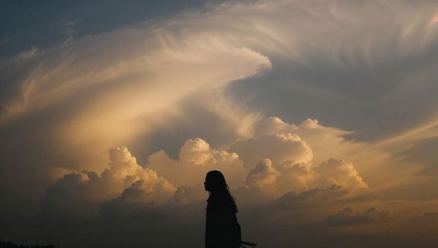 Solitary female silhouette at sunset with golden clouds