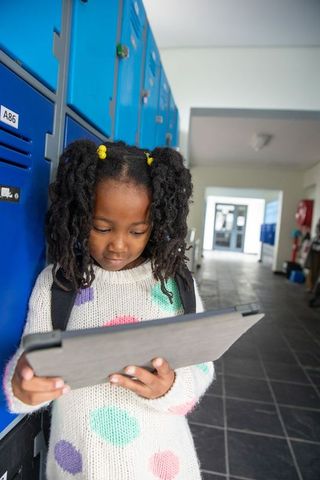Young girl holding tablet in school hallway near blue lockers