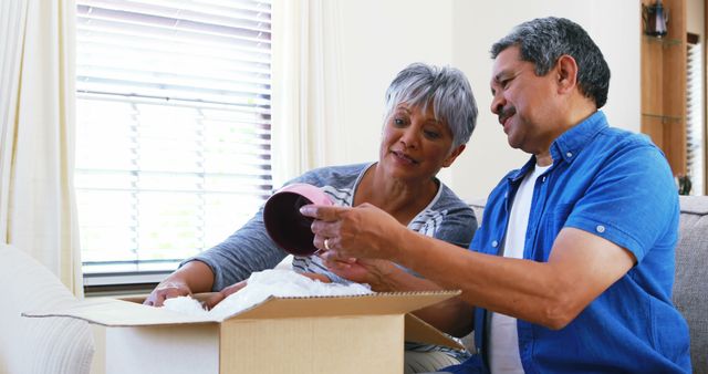 A middle-aged Caucasian couple unpacks household items, with copy space. Their shared activity suggests a sense of togetherness, setting up a new home or organizing belongings.