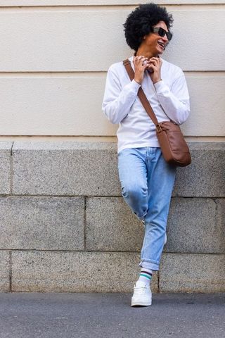African american man leaning on granite ledge smiling wearing sunglasses crossbody bag