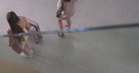 Overhead view two women walking through airport concourse pulling wheeled suitcase carrying bags
