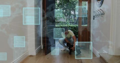 Kneeling asian man greeting small black puppy at open door with futuristic digital hud