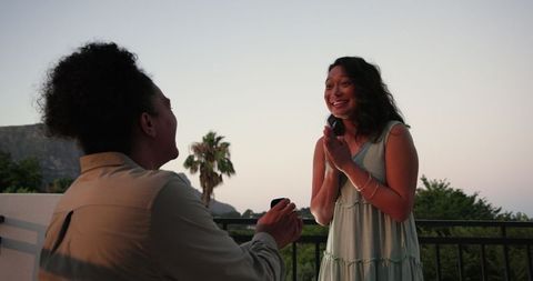 Couple sharing a heartfelt moment on a balcony with a scenic mountain backdrop. Perfect for use in articles or advertisements related to romantic proposals, engagement announcements, love stories, and celebratory moments. Evokes feelings of joy and commitment, highlighting an emotional and joyful occasion in a picturesque setting.