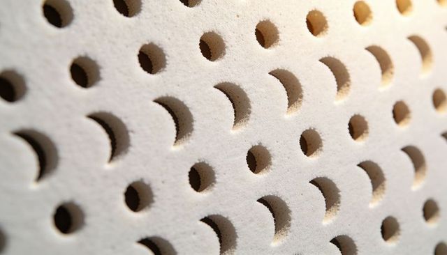 Macro perforated foam panel with diagonal circular holes, porous texture and deep shadows