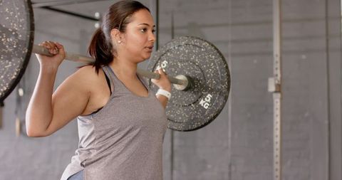 Female athlete performing back squat with barbell and speckled plates in power rack