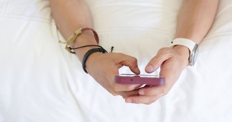 Overhead male hands typing on pink smartphone with braided bracelets and white smartwatch