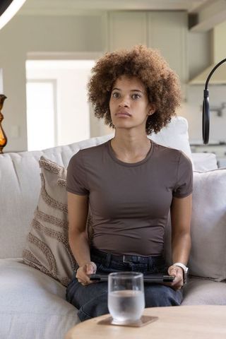 African american woman streaming on couch holding tablet with ring light visible