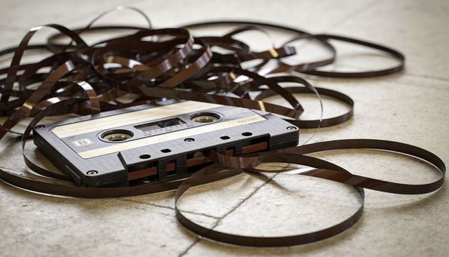Unraveled cassette tape looping across tiled floor, vintage analog music nostalgia closeup