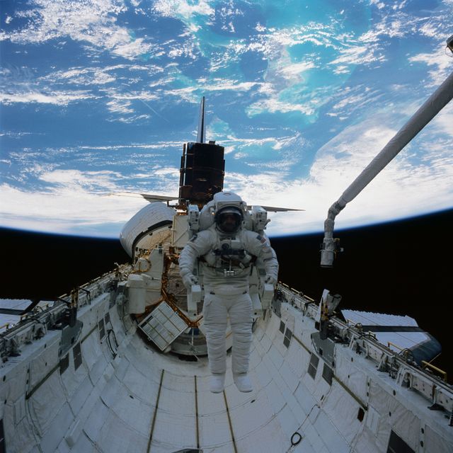 41C-37-1718 (11 April 1984) --- Astronaut James D. van Hoften and a repaired satellite are captured by a Hasselblad camera aimed through Challenger's aft cabin windows toward the cargo bay of the Earth orbiting Challenger.  Dr. van Hoften is getting in his first "field" test of the manned maneuvering unit (MMU) after months of training in an underwater facility and in a simulator on Earth.  The Solar Maximum Mission Satellite (SMMS), revived and almost ready for release into space once more, is docked at the flight support system (FSS).