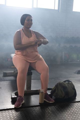 African american woman sitting on bench checking watch in gym workout rest and recovery