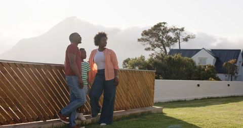 African american family standing on suburban lawn by wooden fence with mountain backdrop