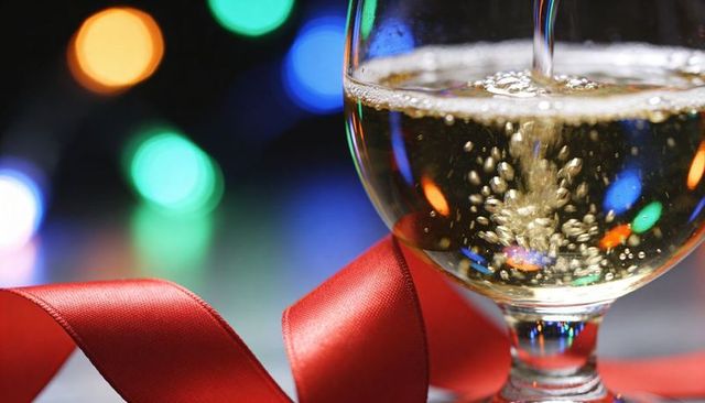 Pouring champagne into stemmed glass with festive bokeh lights and red ribbon
