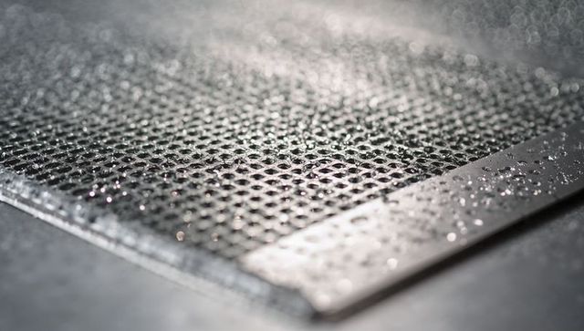 Perforated metal mesh glistening with water droplets, macro honeycomb texture