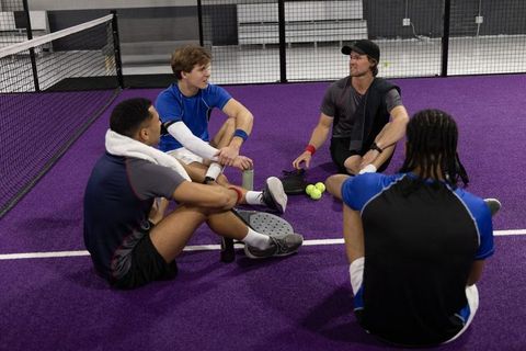 Diverse padel team taking break on purple court during coaching session, team bonding