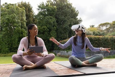 Women practicing outdoor yoga using virtual reality headset and tablet for mindful wellness