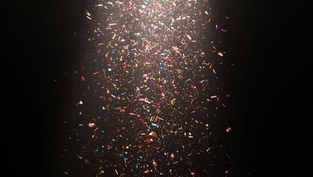 Colorful metallic confetti falling through spotlight on dark stage background