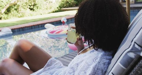African woman relaxing by pool with refreshing lime drink and colorful float in backyard