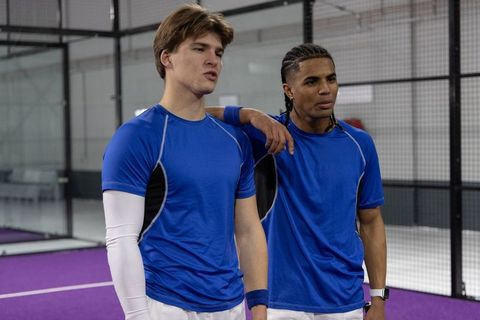 Diverse male athletes standing on indoor racket court in blue shirts showing teamwork