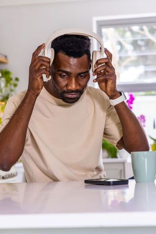 African man putting on headphones at kitchen counter while looking at smartphone