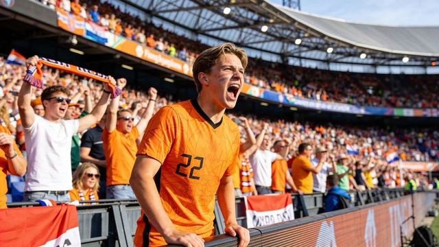 Cheering dutch football fan wearing orange jersey number 22 leaning on barrier amid crowd