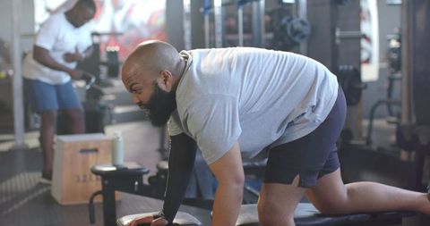 African man powering through bench dumbbell row with compression sleeve in modern gym