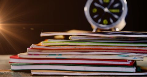 Glowing alarm clock resting on colorful stack of books