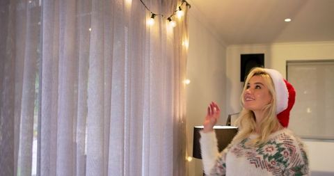 Cozy holiday scene with fairy lights on sheer curtains and woman wearing Santa hat