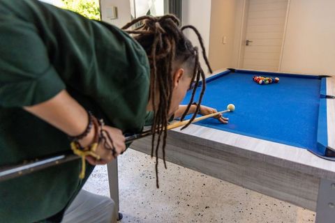 African american man playing pool on blue felt table in bright home game room with dreadlocks