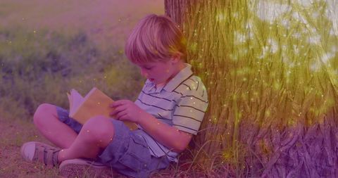 Young boy reading under tree sparkling with magic