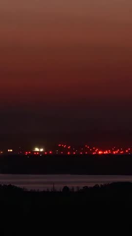 Vertical dusk video showing pulsing red beacons and white lights reflecting on water