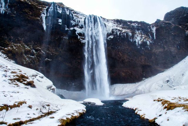 This image captures a majestic waterfall in a wintery setting, surrounded by snow and ice. The cascading water contrasts beautifully with the whiteness around, making it an ideal subject for nature and travel-related content. Suitable for promoting winter tourism, environmental awareness campaigns, and scenic guides. Great for websites, presentations, and social media posts highlighting natural beauty and ecological themes.