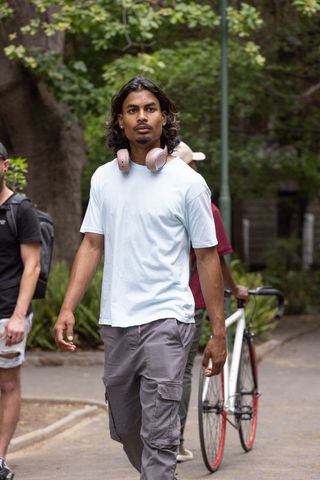 African american man walking in park wearing rose-gold headphones and cargo pants
